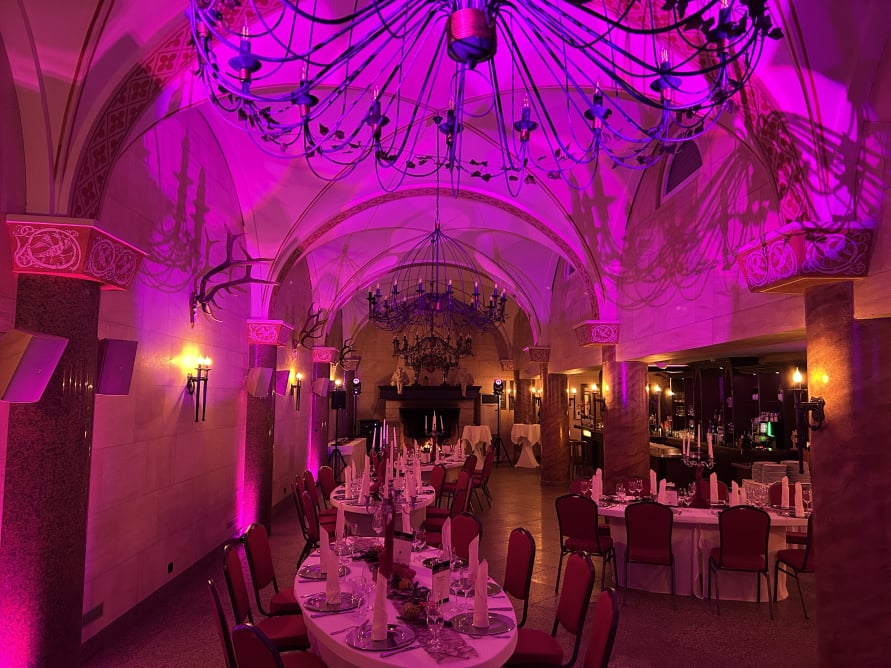 Eventsaal im The Lakeside Burghotel Strausberg mit pinker Ambientebeleuchtung und festlich gedeckten Tischen bei einer Firmenfeier